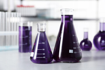 Different laboratory glassware with purple liquid on light table indoors, selective focus