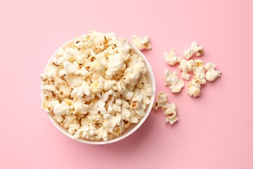 Tasty popcorn in bowl on pink background, flat lay