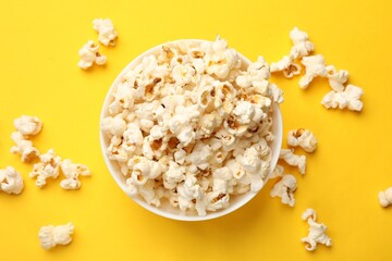 Tasty popcorn in bowl on yellow background, flat lay
