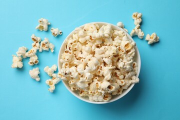 Tasty popcorn in bowl on light blue background, flat lay