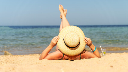 Fototapeta premium A woman in a hat is dried up on the beach