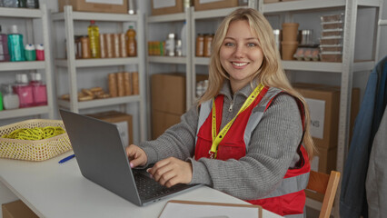 Young caucasian woman volunteer working on laptop in charity donation center organizing supplies...