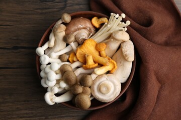 Different raw mushrooms in bowl on wooden table, top view