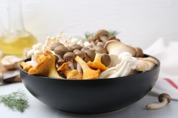 Different raw mushrooms in bowl on white tiled table, closeup