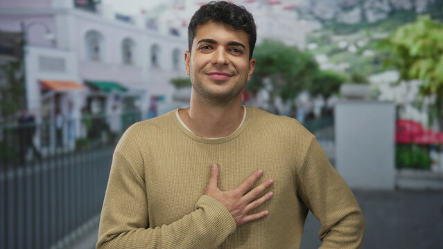 Man lifts hand placing it on chest using palm in outdoor hispanic young scene showing gratitude sincerity.