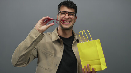 Man wearing glasses is pulling a paper bag in a studio with hispanic young colored background and showing male specs clearly.