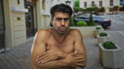 Obraz premium Man bares muscular arms and crosses them tightly under his chin on an empty city street as he shivers in the cold; cold discomfort.