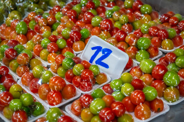 Vibrant mix of green, yellow, orange, and red tomatoes packed in foam trays wrapped in plastic,...