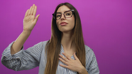 Woman holds hand to chest and raises palm against vibrant magenta studio backdrop with closed eyes...