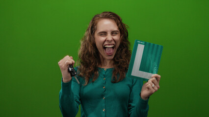 Woman celebrating holding car keys and learner sign against isolated green background with joy and excitement.