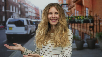 Confident woman with hand raised presenting street scene captures a blonde young model smiling against an urban outdoor city backdrop.