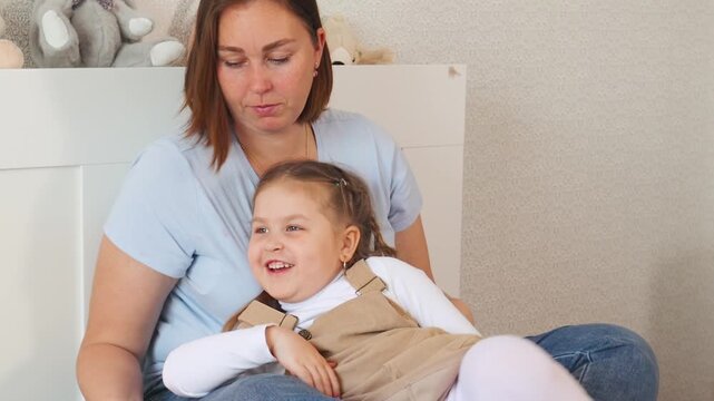 Woman and Caucasian daughter enjoy reading on a soft bed at home. Learning moment filled with comfort, trust, and early cognitive stimulation