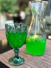 Green beverage in glass and carafe on table. Lemonade or cocktail with citrus and ice, refreshing summer drink for café, bar or restaurant, concept of healthy lifestyle and wellness