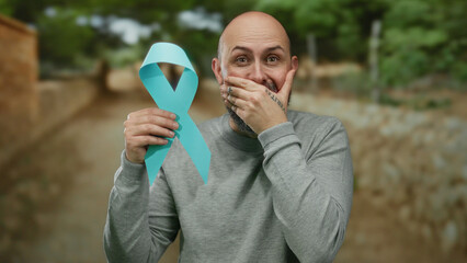 Man with beard holding blue ribbon outdoors expressing surprise in a park setting, symbolizing...