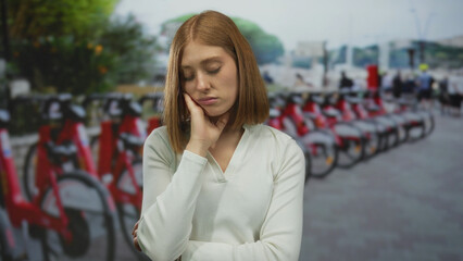 Woman contemplating in an urban street surrounded by parked bicycles conveying a sense of...