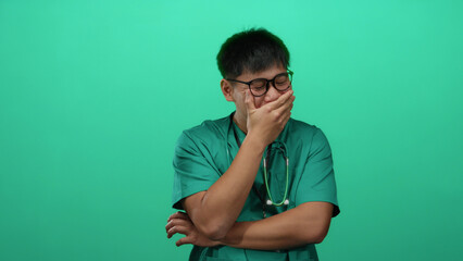 Young chinese man in a green medical uniform laughing joyfully over an isolated green background...