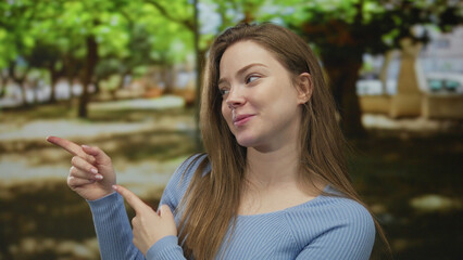 Woman pointing finger along a leafy forest path wearing a blue sweater with a slight smile; playful...