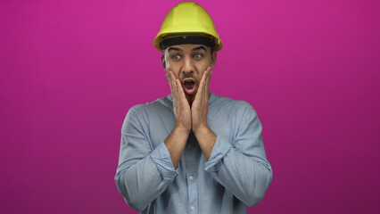 Young hispanic man wearing hardhat expresses surprise over isolated pink background, conveying a...