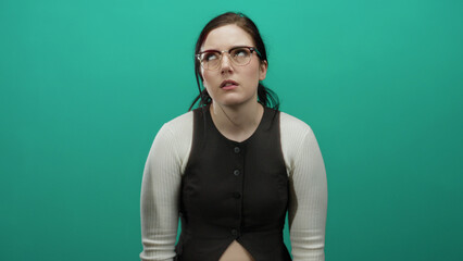 Fototapeta premium Woman with glasses and brunette hair expressing emotion against a green background, featuring casual attire and white sleeves in a close-up shot.