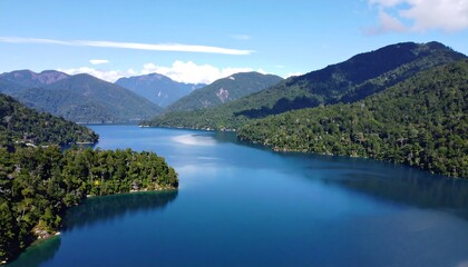 Fototapeta premium Serene Lake Surrounded by Lush Green Mountains Under a Clear Blue Sky.