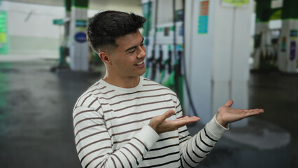 Young man pointing and smiling at a petrol station, conveying energy and confidence with his casual outfit.