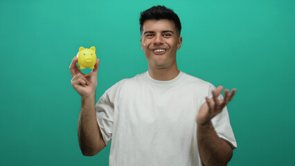 Young man holding yellow piggy bank smiling against green background showing happiness and...