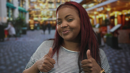 Woman smiling and giving thumbs up hand gesture on busy city street lined with stores and...
