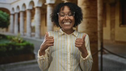Woman points finger at camera in old building while smiling broadly and giving thumbs up gesture;...