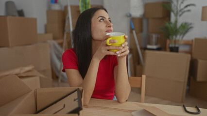 Woman smiling while holding a yellow cup surrounded by cardboard boxes in a cozy new apartment...