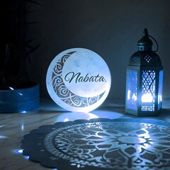 "A softly illuminated decorative scene with an Islamic-inspired ambiance. A glowing crescent moon-shaped lamp hangs, with elegant calligraphy text inside it. Beside it, a traditional ornate lantern em