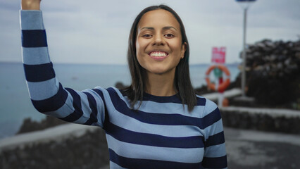 Young woman smiling on a seaside promenade with ocean backdrop, embodying joy and serenity in the...