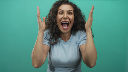 Woman covering eyes with hands and laughing in green studio while wearing light blue shirt;...