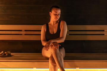 Woman seated on sauna bench, calm cozy mood, warm light. Relax in steamroom.