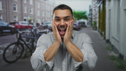 Fototapeta premium Young hispanic man pressing hands to cheeks for toothache on street lined with bicycles and buildings; pain.