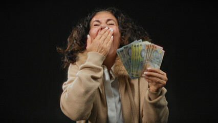 Middle-aged woman joyously holding romanian banknotes against isolated black background, expressing...