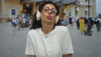 Woman sends a kiss and forms a finger heart gesture with her fingers on a busy city sidewalk;...