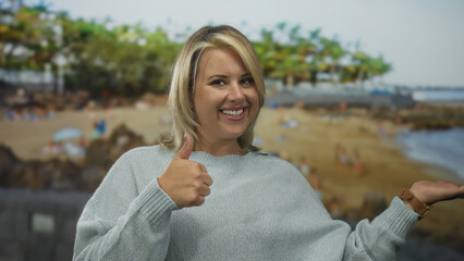 Woman smiles and makes thumbs up gesture and holds open palm to side presenting space in studio...