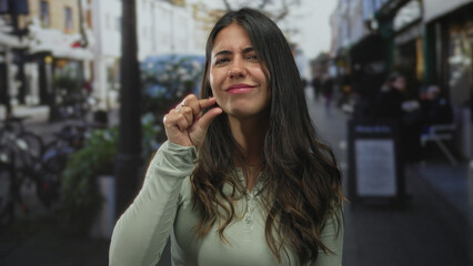 Woman pinches fingertips together making a small gesture on street while smiling subtly; playful...