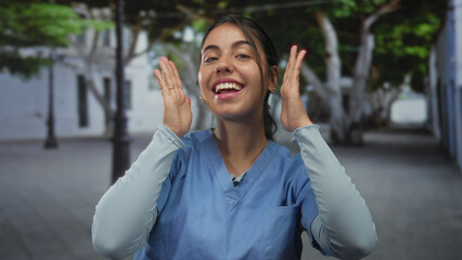 Young hispanic woman framing her smiling face with both hands on busy street; playfulness creativity curiosity.