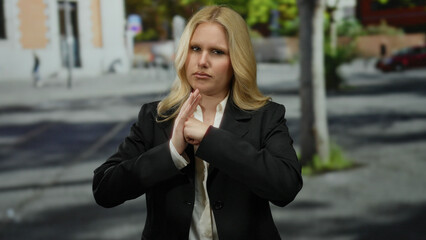 Young blonde woman on city street makes a fight gesture with a serious expression, surrounded by...