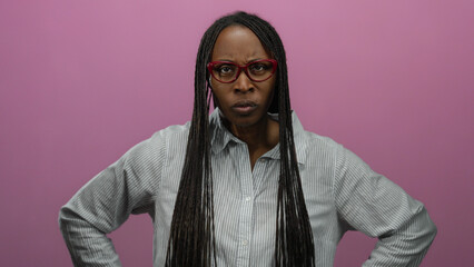 Woman with glasses and braids stands in front of an isolated pink background wall expressing...
