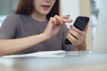 Young asian business woman in casual clothes using mobile phone, searching the information, online working on laptop computer at home office. remote work. Student studying online, e-learning