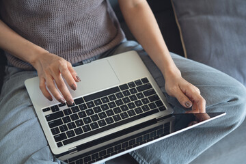 Close up, woman sitting on a couch at home, using laptop on her lap surfing the internet, remote...