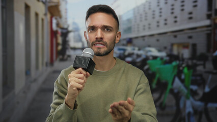 Young man with microphone conducting interview on urban street with city background