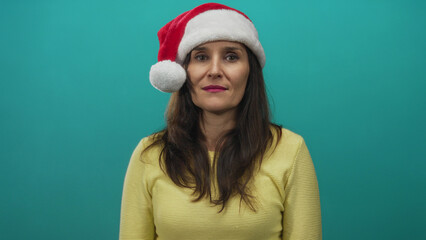 Woman in yellow sweater wearing christmas hat smiles excitedly against bright green wall, capturing festive joy and holiday spirit in an isolated setting.