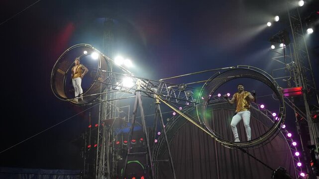 Funny acrobats in the rotating wheel of death, performing under the dome of the circus in the light of bright concert lights and smoke. Acrobats dance in an acrobatic wheel.