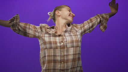 Woman in plaid shirt stretching her bare arms wide with closed eyes and subtle smile in a vivid purple studio scene; tired.