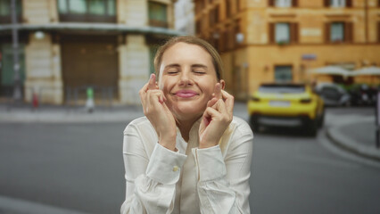 Woman crossing fingers on a city street outdoors showing hope luck expectation success blonde white...