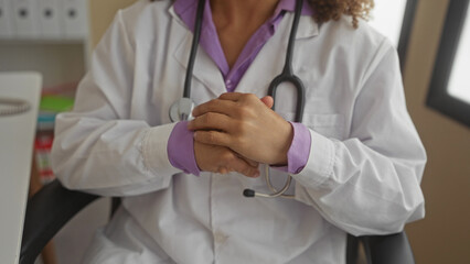 Hispanic transgender woman doctor wearing a lab coat and stethoscope rubbing hands in clinic...