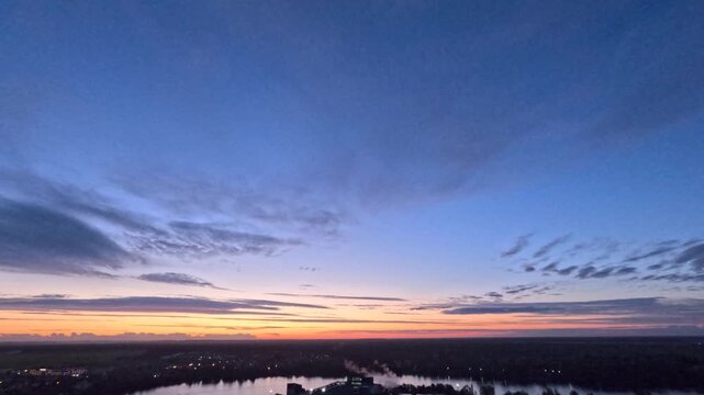 Beautiful view of the colorful sunset sky and moving clouds over the river landscape with forest on the horizon. Time lapse shows change from evening to night